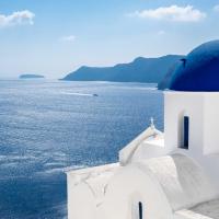 white greek church with blue dome faces blue sea on a bright sunny day 
