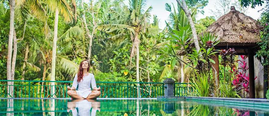 Woman meditating poolside at luxury resort in Bali
