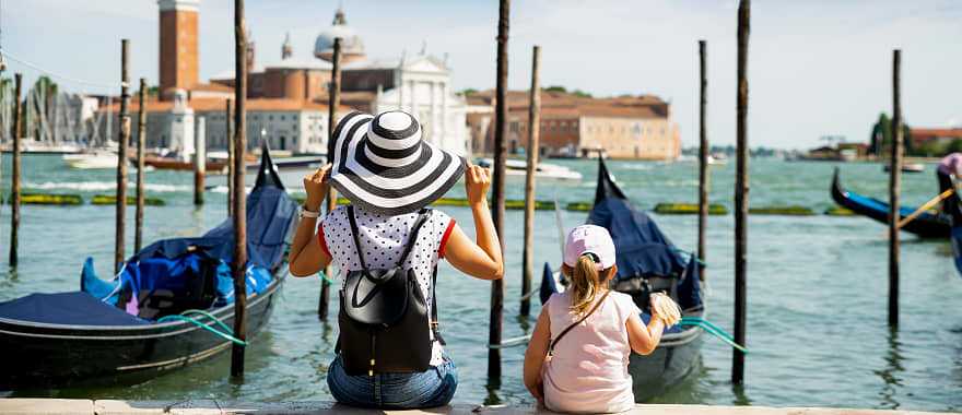 Mother and daughter sitting in front of gondolas looking at San Giorgio Maggiore in Venice, Italy