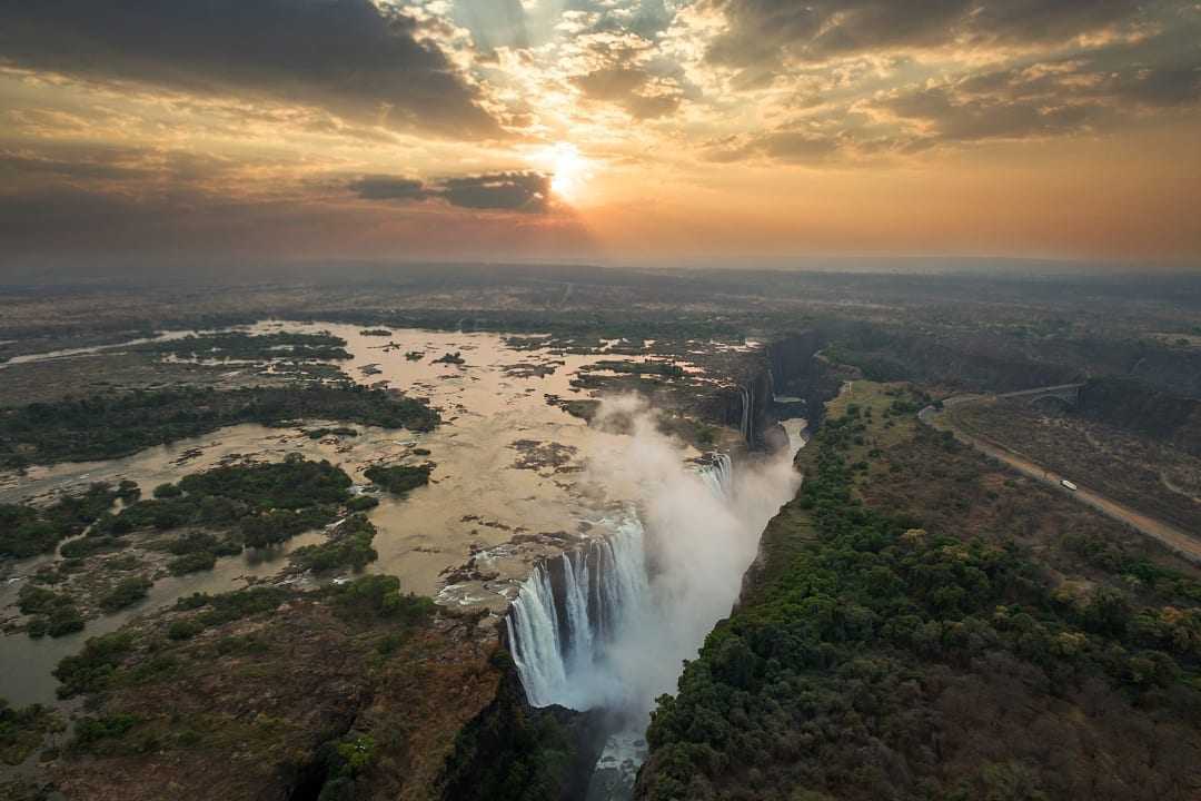 The mighty Victoria Falls cascades dramatically at sunset over Zambezi River.