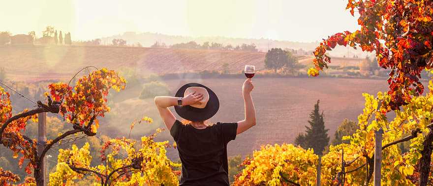Woman raising a glass of wine, enjoying the view at sunset in Tuscany