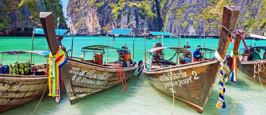Wooden boats in the turquoise waters of Maya Bay with limestone karst cliffs on Phi Phi island in Thailand