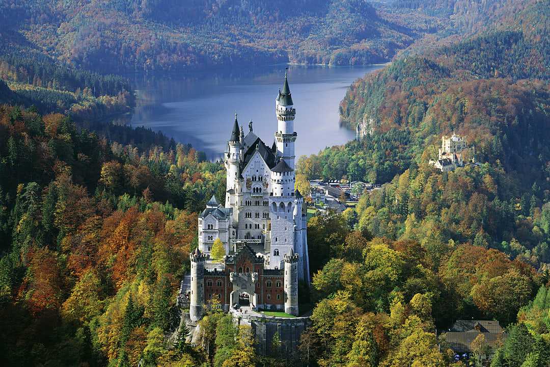 Neuschwanstein Castle in Bavaria, Germany, surrounded by autumn forest and overlooking a mountain lake