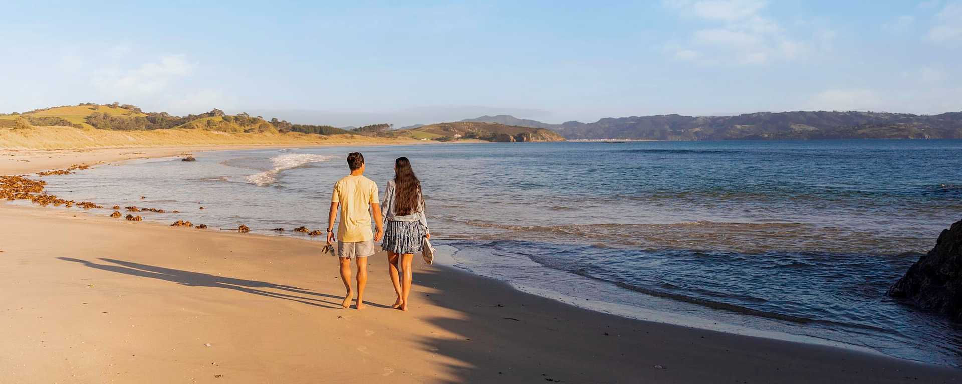 Couple walking on Tawharanui Beach in Auckland New Zealand