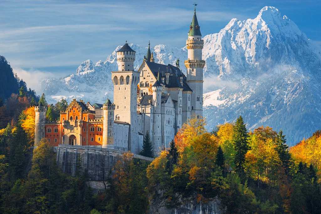 Neuschwanstein castle surrounded by trees with autumn colors and snowcapped mountain