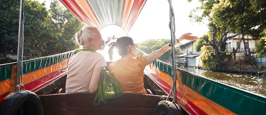 Senior travelers riding a colorful longtail boat through a canal at sunset in Bangkok, Thailand