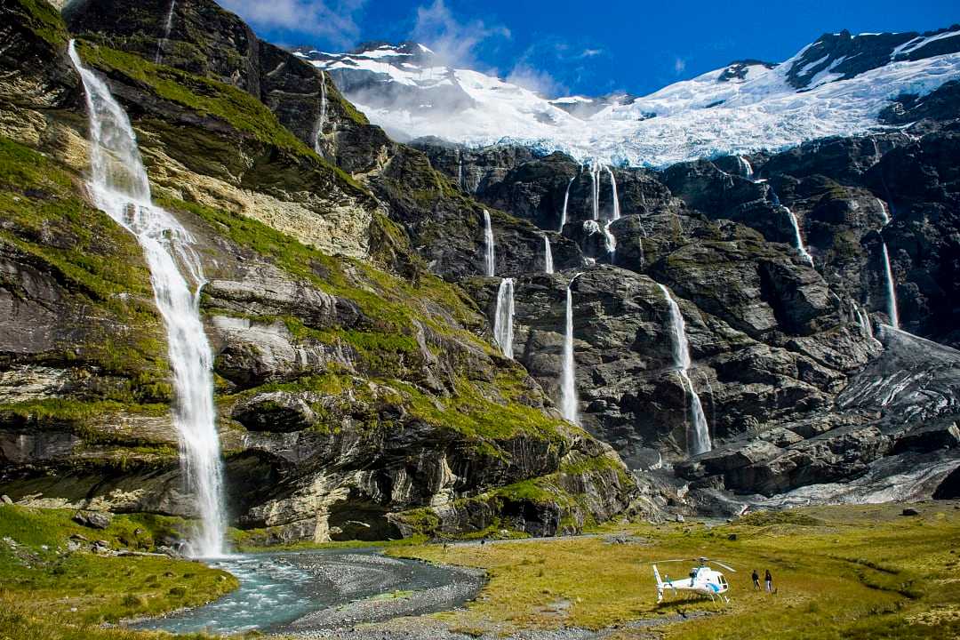 Couple heli hiking at Earnslaw Burn with hanging glacier and cascading waterfalls 