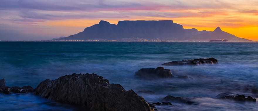 Silhouette of Table Mountain against sunset sky and ocean waves in Cape Town, South Africa
