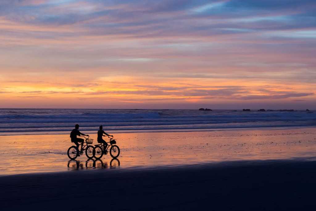 Couple biking on the beach at sunset in Costa Rica