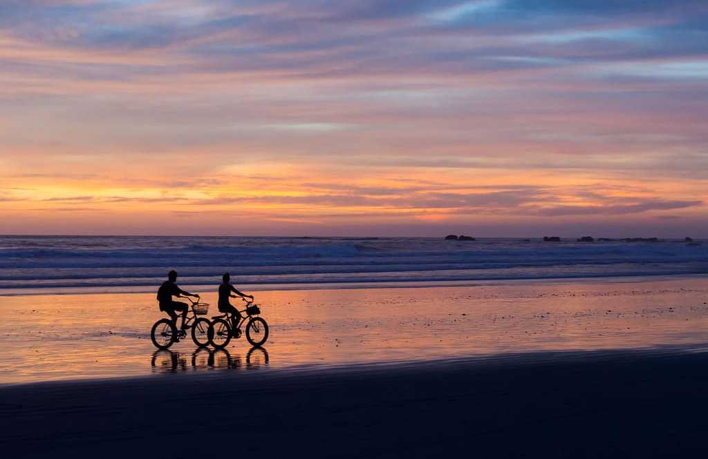 Couple biking on the beach at sunset in Costa Rica Couple biking on the beach at sunset in Costa Rica