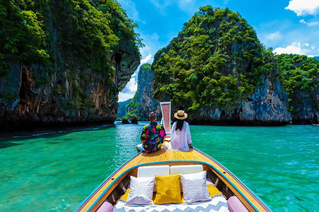 Couple on a traditional boat exploring turquoise waters and limestone cliffs in Krabi, Thailand