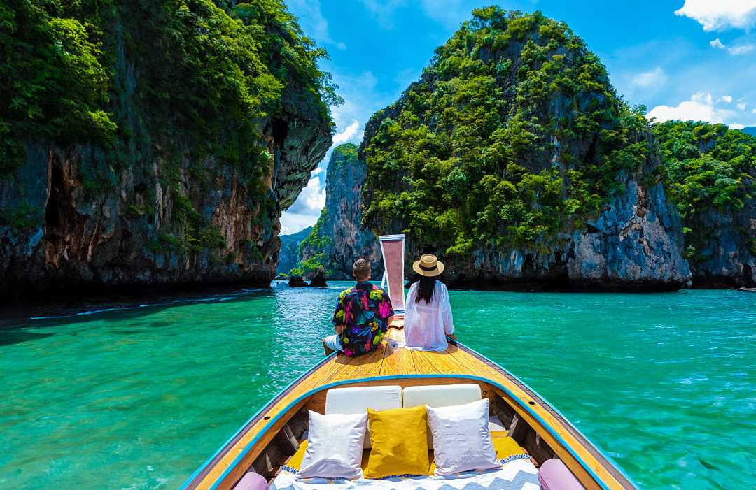 Krabi, Thailand Couple on a traditional boat exploring turquoise waters and limestone cliffs in Krabi, Thailand