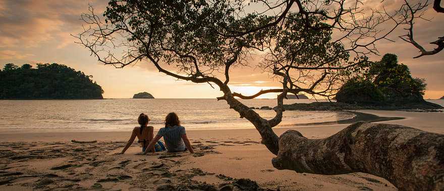 Couple sitting on the beach watching the sunset in Manuel Antonio National Park