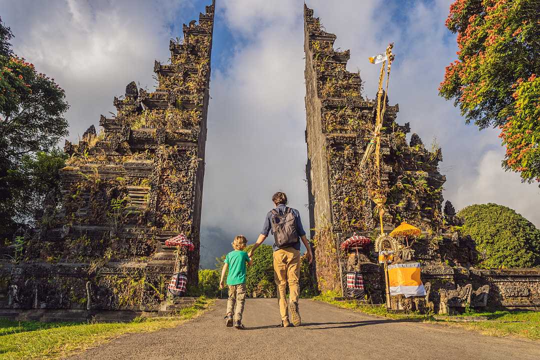 Father and son walking through traditional balinese gate Candi Bentar in Bali, Indonesia