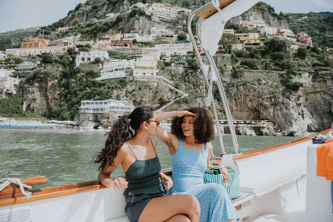 Two women enjoying a boat ride along the Amalfi Coast, Italy, with colorful cliffside villages in the background