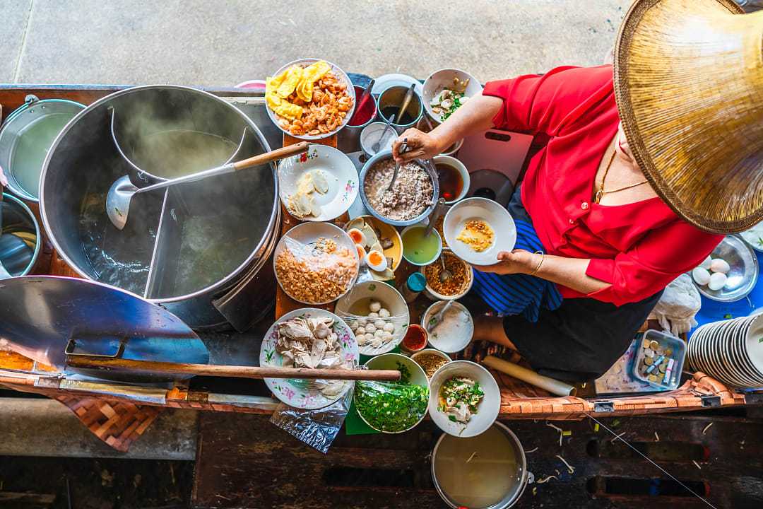 Woman preparing Thai noodle soup Tom Yum on boat in local floating market in Bangkok, Thailand