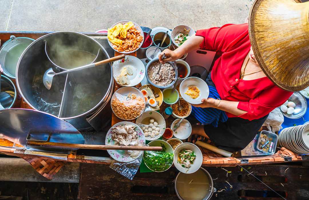 Woman preparing Thai noodle soup Tom Yum on boat in local floating market in Bangkok, Thailand