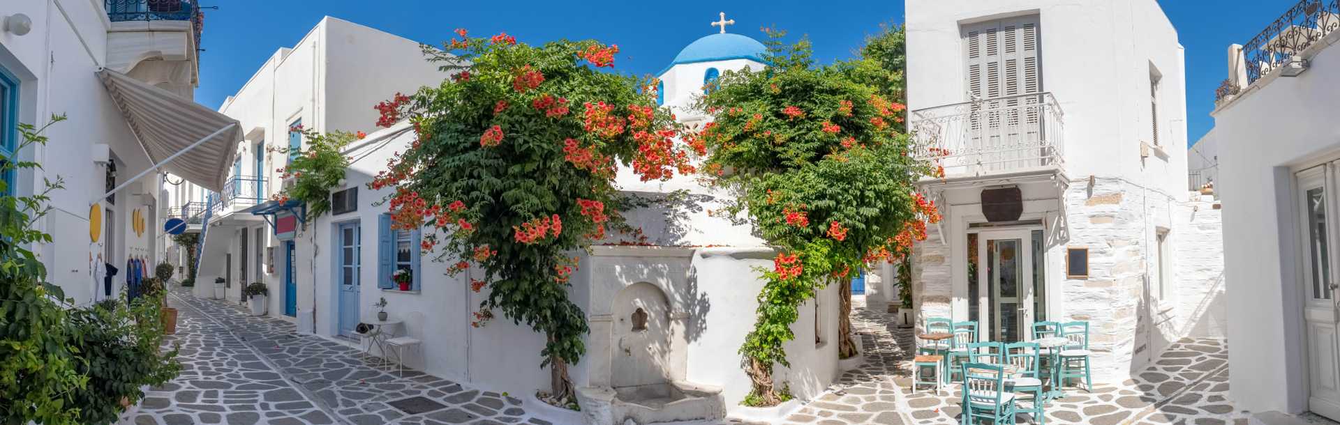 Narrow street in Greece with cozy outdoor cafe and traditional greek church in Parikia village on Paros island, Cyclades.