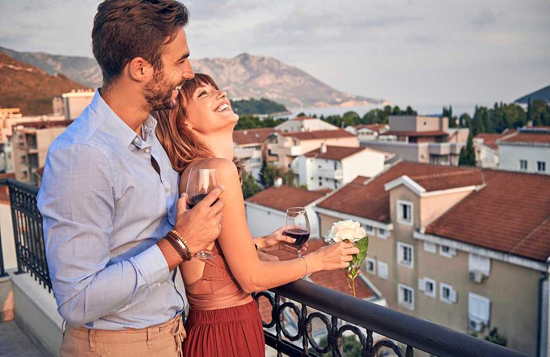 Smiling couple embracing on a balcony overlooking a coastal town.