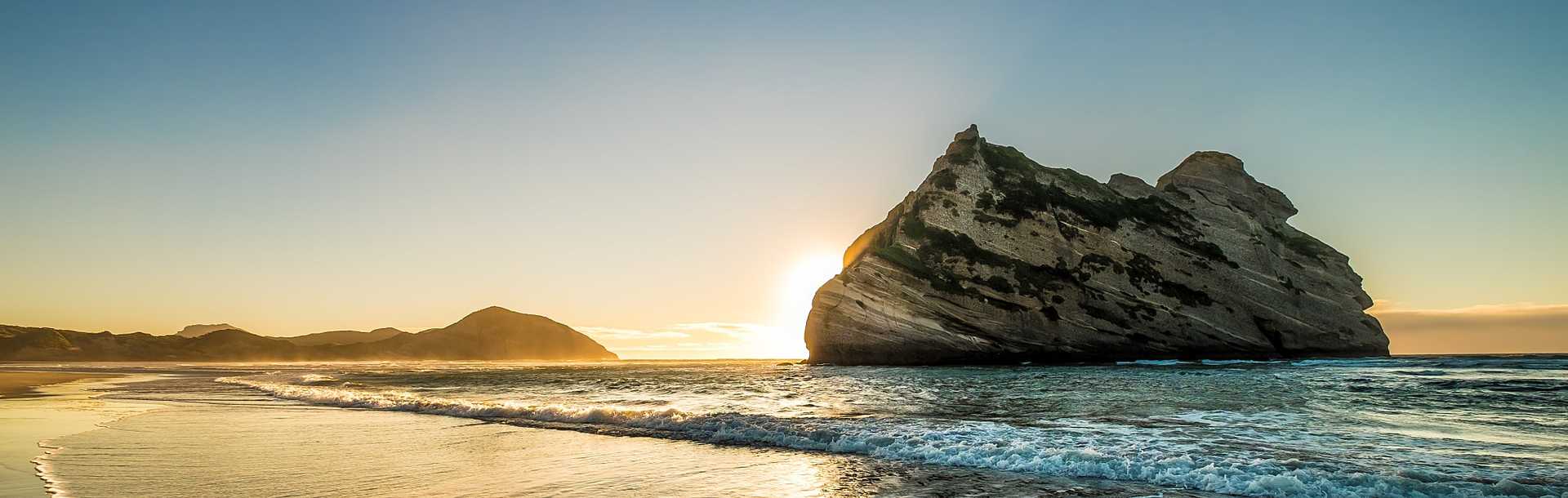 Sun rising behind the rock formation at Wharariki Beach on the South Island of New Zealand.