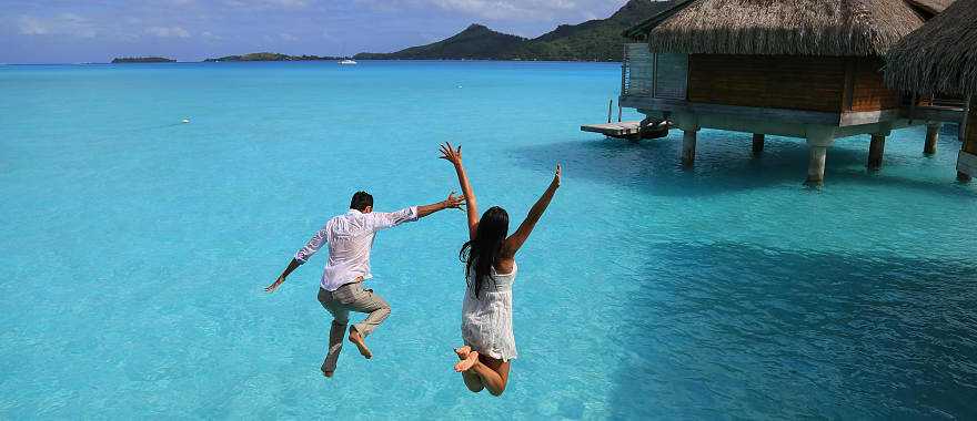 Happy young couple jump into the water from their over water bungalow in Bora Bora