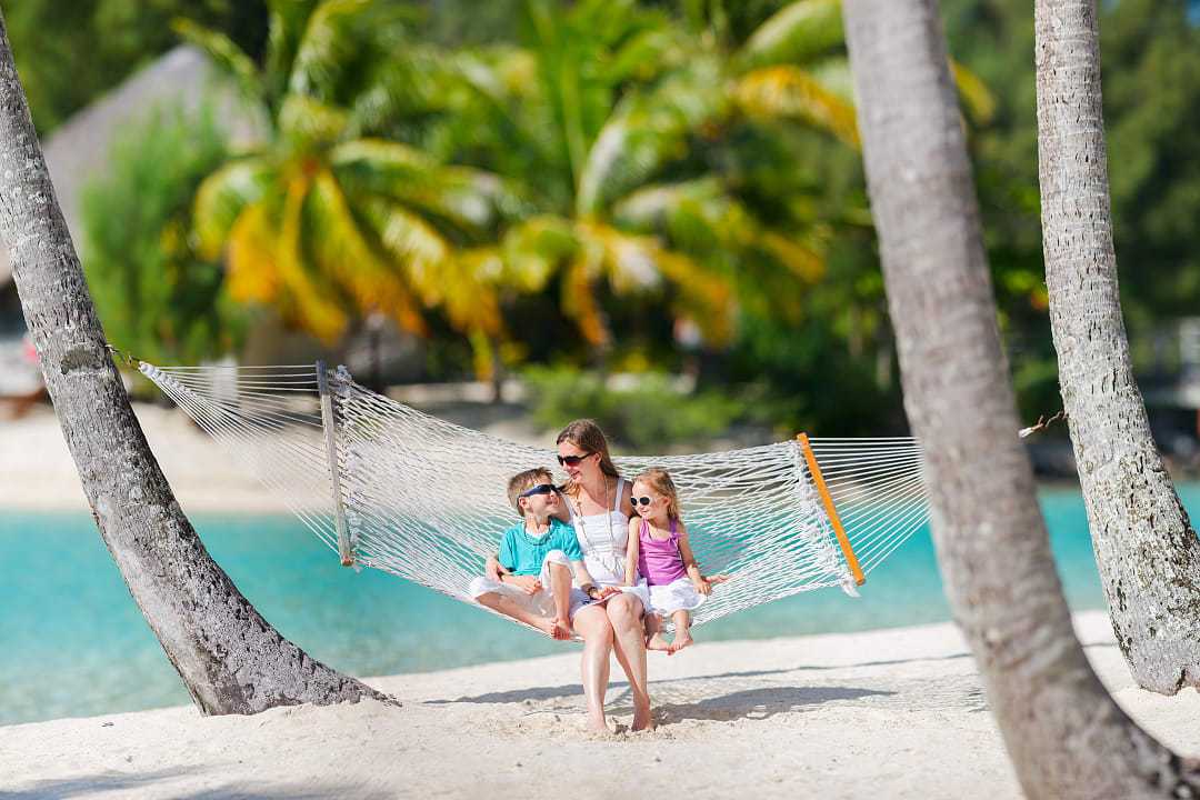 Mother swinging in a hammock on the beach with her kids in French Polynesia