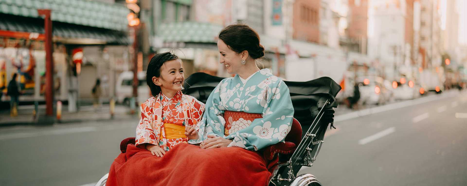 mother and young daughter in kimono, enjoying rickshaw ride while on vacation in tokyo, japan