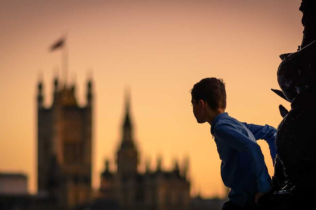 Child climbing a lamp post in south bank in london (uk) at sunset with the houses of parliament in the background