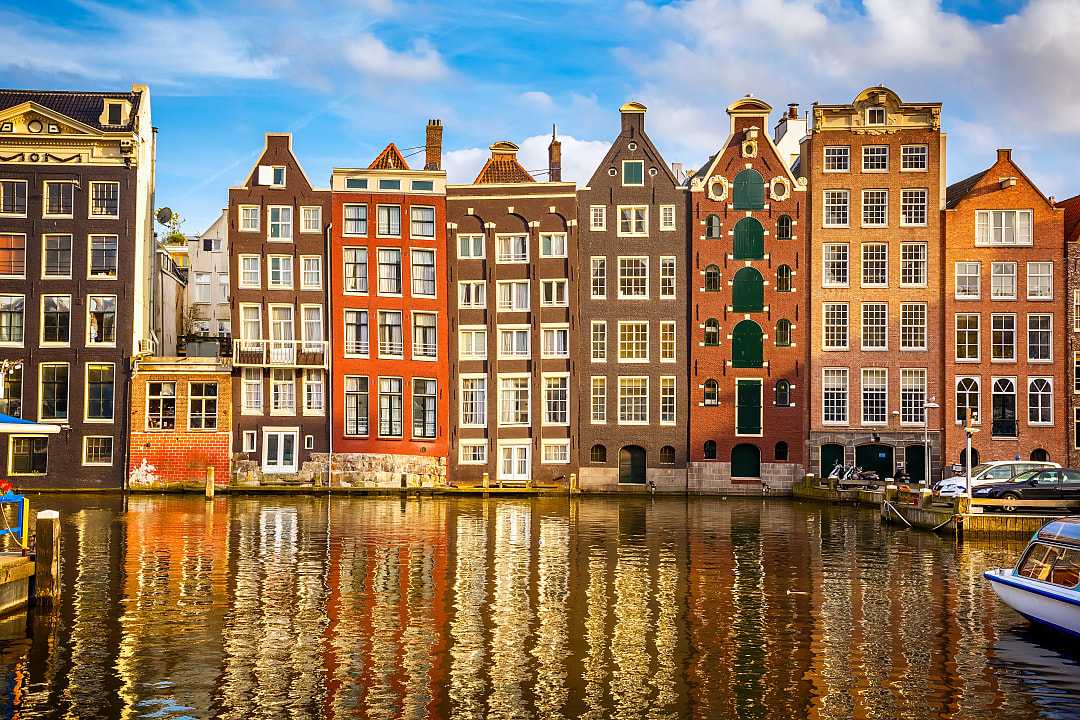 Amsterdam’s colorful canal houses reflect beautifully on the calm water.