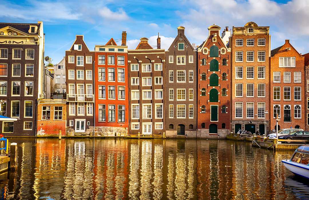 Amsterdam’s colorful canal houses reflect beautifully on the calm water.