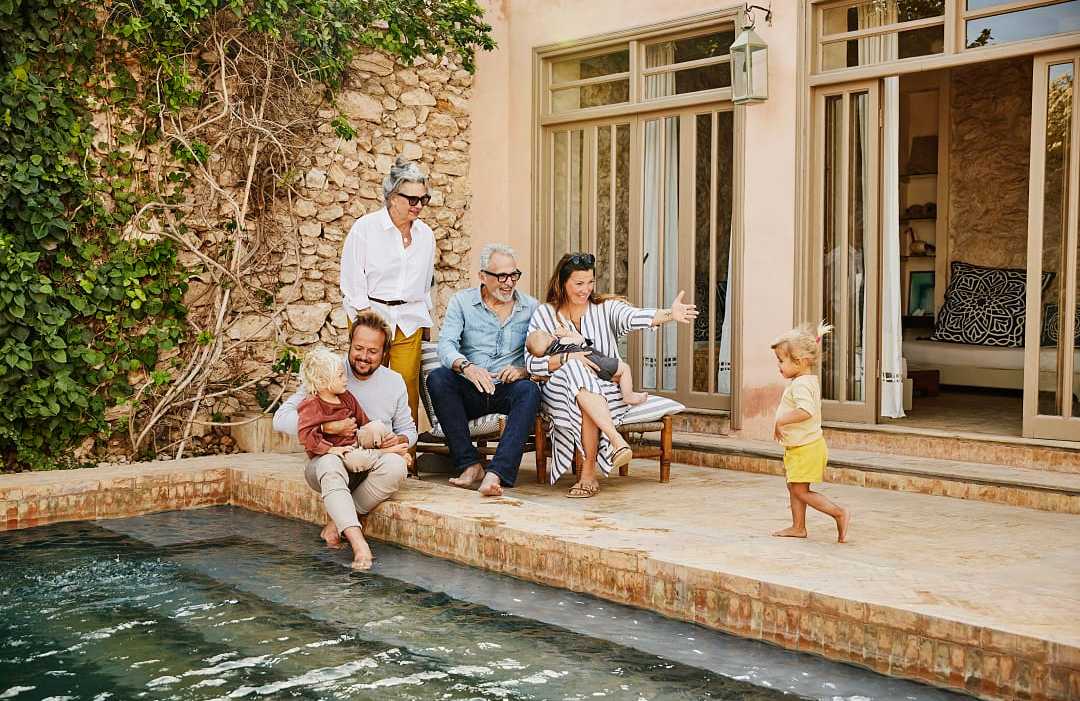 Smiling grandparents relaxing with children and grandchildren beside pool at villa during multigenerational family vacation