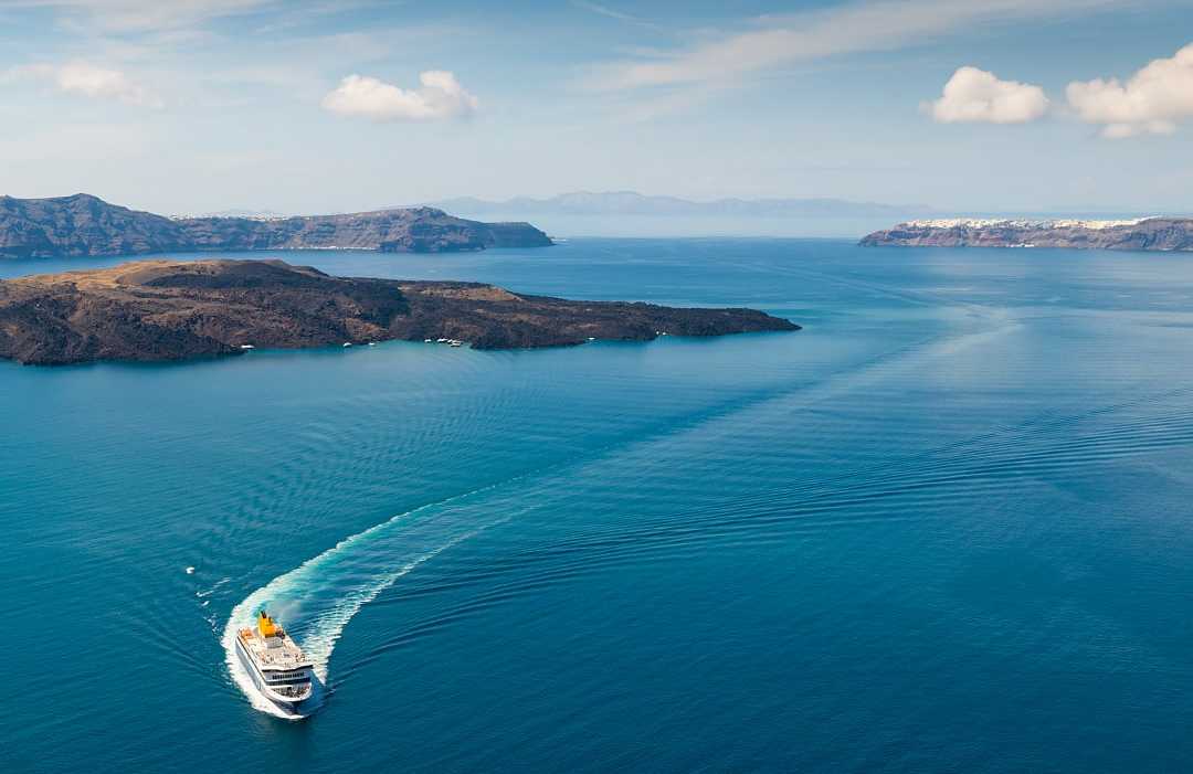 Santorini, Greece White ferry boat cruising through deep blue water near islands.