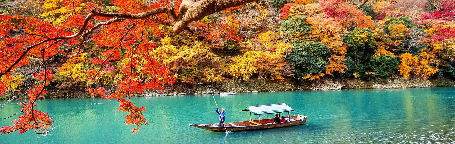 Boatman punting a boat down river in Arashiyama during the autumn season in Kyoto, Japan.