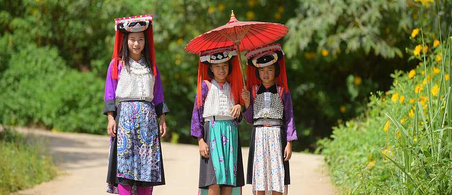 Three young Lahu Tribe girls in custom dress, smiling among the sunlight in Thailand.