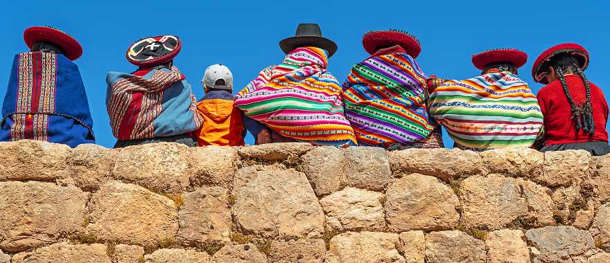 Native Peruvian women pose on a rock wall with a young tourist in Cusco