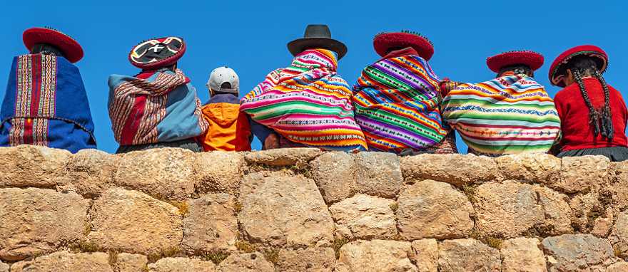 Cusco, Peru Native Peruvian women pose on a rock wall with a young tourist in Cusco
