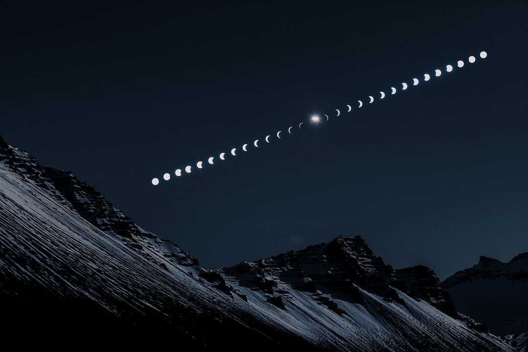 Composite image showing the phases of a solar eclipse over snow-covered mountain peaks at night.
