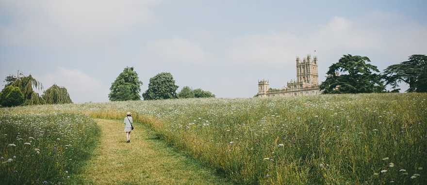 Visitor walking toward Highclere Castle through a wildflower field in Hampshire, England