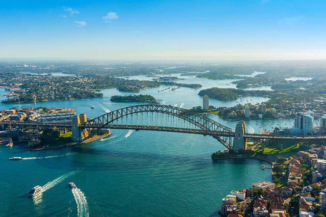 Sydney’s Harbour Bridge stretches proudly across sparkling, boat-filled waters.