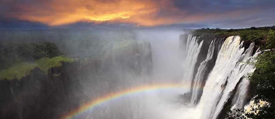 Gorgeous view of Victoria Falls at sunset with a rainbow forming in the mist, Zambia, Africa