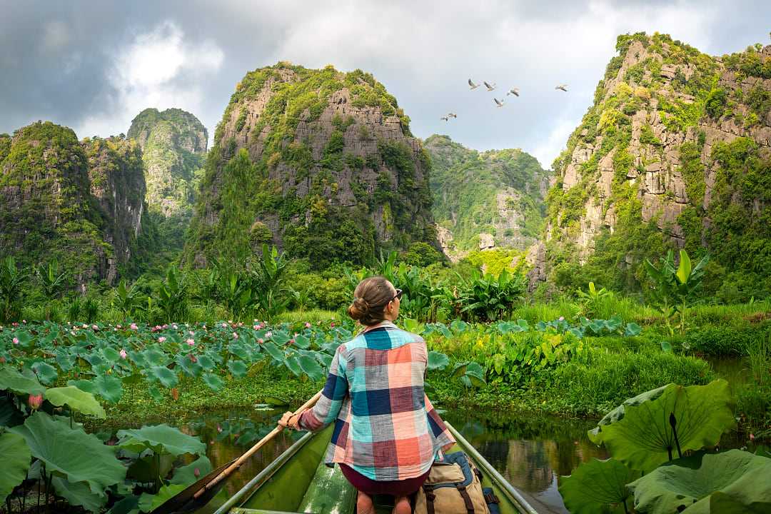 woman travels along river in boat, enjoying picturesque karst mountains in Ninh Binh Province, Vietnam