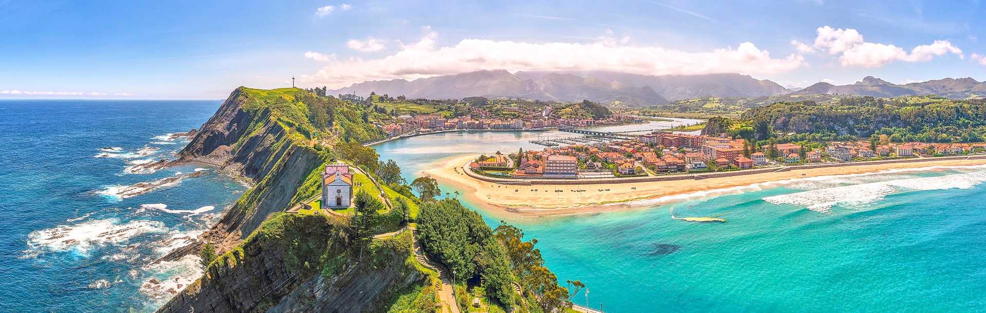 Aerial panorama of a church on top of the cliffs with views of the beach and mountains in Principality of Asturias, Spain.