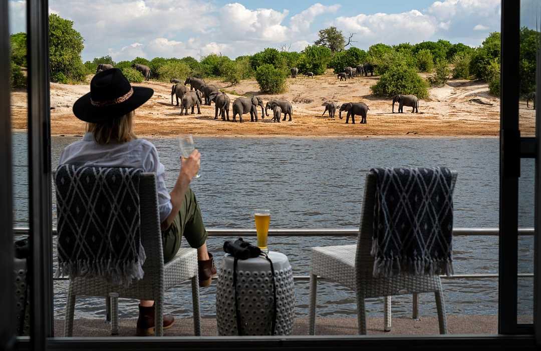Chobe Princesses by Mantis.  Photo courtesy of The Zambezi Queen Collection Woman sitting on the balcony of boat watching elephants on the river bank