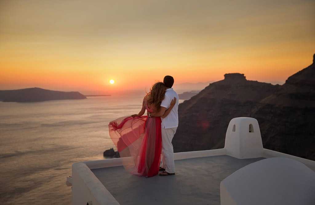 A couple watches the sunset over Santorini, Greece