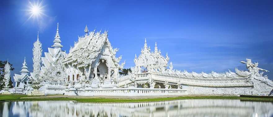Chiang Rai’s Wat Rong Khun, the White Temple, reflected in water with clear blue sky