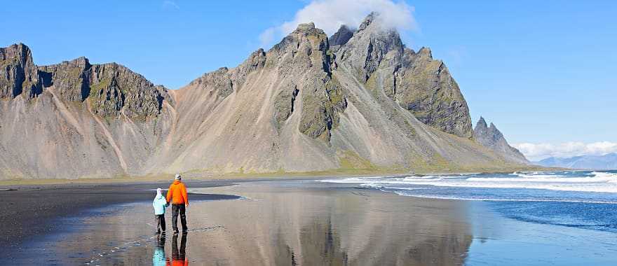 Father and son, walking on black sand beach at beautiful Stokksnes peninsula, enjoying scenery of Vestrahorn mountains in iceland