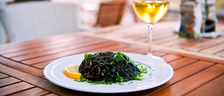 Black risotto with seafood and glass of white wine