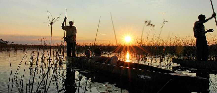 Couple on mokoro boat safari at sunset in the Okavango Delta, Botswana