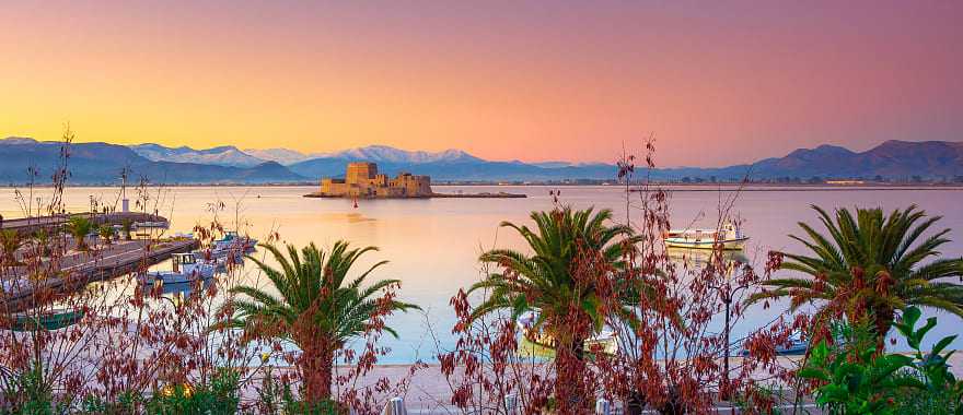 Nafplio Greece with palm trees, boats and Bourtzi castle on the water at sunset