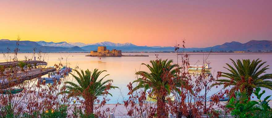 Nafplio Greece with palm trees, boats and Bourtzi castle on the water at sunset Nafplio Greece with palm trees, boats and Bourtzi castle on the water at sunset